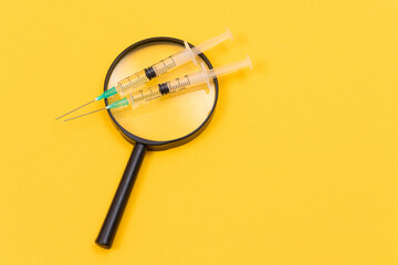 A Magnifier with Medical Syringe Lying on Yellow Table - Vaccination Concept