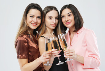 three young beautiful women dressed in pajamas drink champagne and have fun, pajama party and friendship concept.