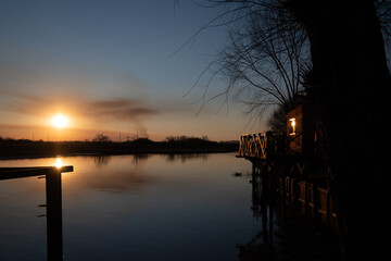 casilla con muelle de madera junto a rio Paraná en atardecer dorado y agua calma 