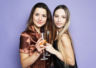 Fototapeta na wymiar two beautiful women dressed in pajamas drink champagne and have fun over purple background