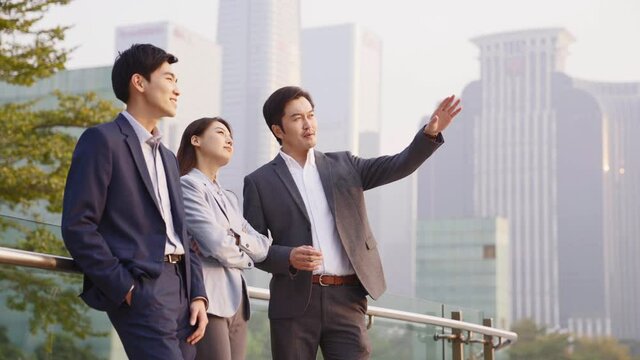 team of asian office workers standing outdoors discussing business in downtown financial district of modern city