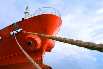 Low angle view of cargo ship docked at port with mooring rope against white clouds on blue sky...