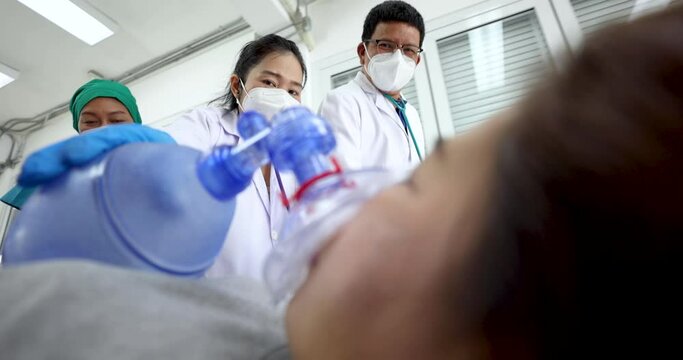 Close up video shot, team of medical person, doctor and nurse, moving female patient on bed, using resuscitator face mask, ambu bag equipment help for breathing in emergency case. Take from low angle.