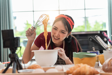 Happy asian woman is cooking cookies and having fun in the kitchen. She making video for her culinary vlog.