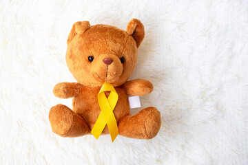 Yellow Ribbon with Bear doll on white background for supporting kid living and illness. September Childhood Cancer Awareness month and World cancer day concept