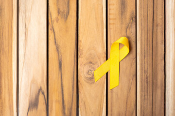 Yellow Ribbon on wooden table background for supporting people living and illness. September Suicide prevention day, Childhood Cancer Awareness month and World cancer day concept