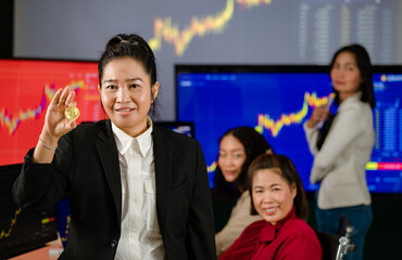 Closeup shot of golden bitcoin electronic token cryptocurrency money in Asian businesswoman hand in trade room with investors monitoring market graph chart on computer screen in blurred background