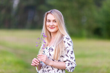 Obraz premium cute blonde woman with a flower in a summer light dress in nature