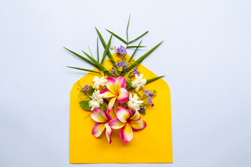 flowers frangipani, jasmine, purple and bamboo leaf arrangement in yellow envelope flat lay postcard style on background white