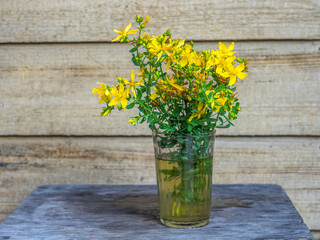 St. John's wort branch in a glass glass on a stool standing on the porch of a country house