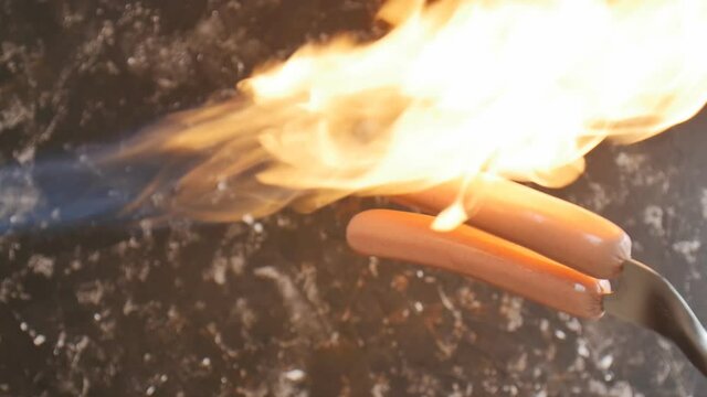 the cook burns hot dog sausages with fire. Two sausages are planted on a kitchen fork and fried with a flame according to the recipe. Slow motion