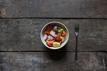 Vegetable green salad prepared with cucumber, tomato, onion and lemon slices in a bowl. A popular healthy food ingredient. Top view.