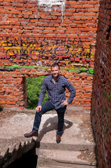 Fototapeta premium Full-length portrait of a young man in a brick house under construction on the stairs
