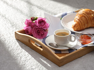Breakfast on a wooden tray with coffee, croissants, jam, flowers and paper note, close up shot