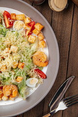 Caesar salad with shrimp and croutons on wooden background