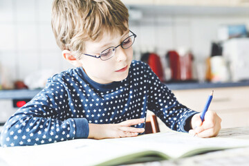 Cute little kid boy with glasses at home making homework, writing letters with colorful pens....