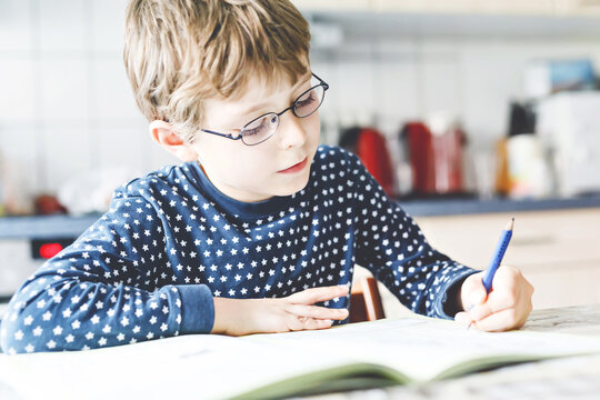 Cute little kid boy with glasses at home making homework, writing letters with colorful pens. Little child doing excercise, indoors. Elementary school and education, imagine fantasy concept