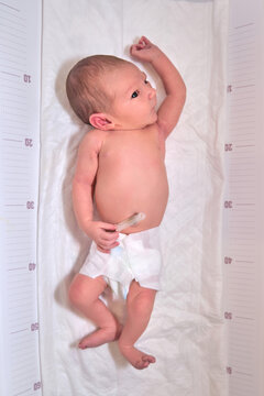 A newborn baby in diapers on a white changing table with a ruler for measuring full-length