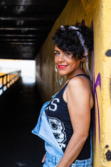 Mid adult afro mexican smiling woman leaning against a wall at the entrance of a tunnel