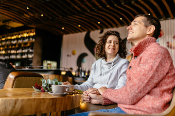 Pregnant woman and man with coffee cups drinking in cafe, talking, warming after walking in cold weather. Pregnancy, parenthood and people concept.