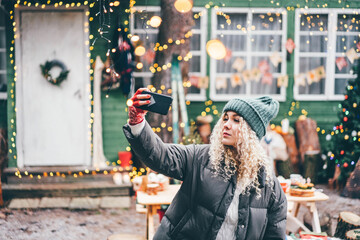 Portrait of smiling woman making selfie. Festive Christmas fair on background.