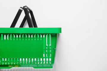 Fototapeta premium Green plastic shopping basket with black handles, retail commerce and consumerism concept, isolated on white background
