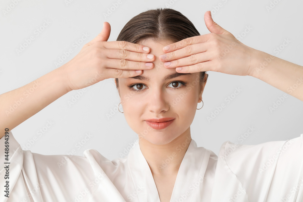 Wall mural Beautiful young woman massaging her face on light background