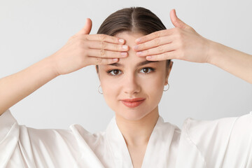 Fototapeta premium Beautiful young woman massaging her face on light background