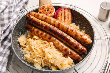 Frying pan with tasty sauerkraut and grilled sausages on light background, closeup