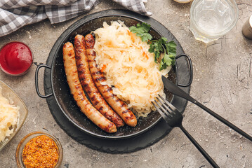 Frying pan with tasty sauerkraut, grilled sausages and sauces on grunge background