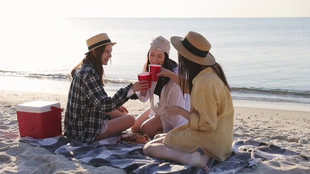 Three friends young women in straw hat summer clothes have picnic hanging out drink liguor having fun raise toasts isolated on sea beach background outdoors. People vacation lifestyle journey concept