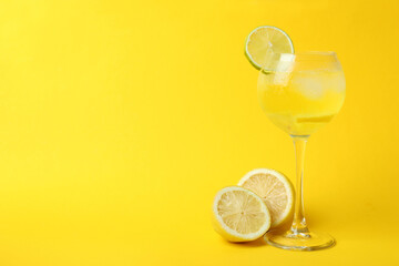 Glass of lemon cocktail and ingredients on yellow background