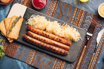 Board with tasty grilled sausages, sauerkraut, crispbreads and sauce on color background