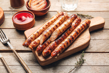 Board with tasty grilled sausages and sauce on wooden background