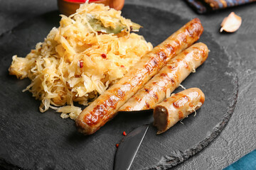 Slate plate with tasty sauerkraut and grilled sausages on dark background, closeup