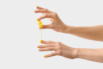 Woman with beautiful manicure pouring nail polish onto fingers on light background