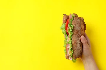 Wandaufkleber Female hand holds ciabatta sandwich on yellow background © Atlas