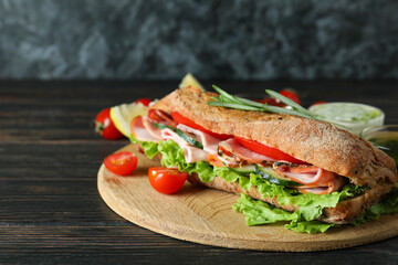 Board with ciabatta sandwich and ingredients on wooden table