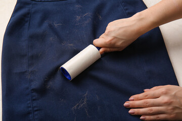 Woman cleaning clothes with lint roller on light background, closeup