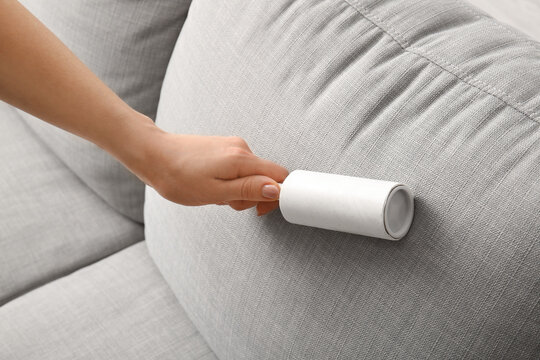 Woman cleaning sofa with lint roller, closeup