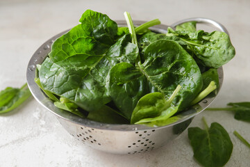 Colander with fresh spinach leaves on light background, closeup