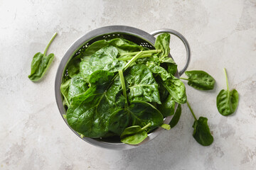 Colander with fresh spinach leaves on light background