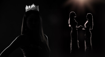 Portrait of Miss Pageant Beauty queen Contest in sequin Evening Ball Gown long dress with sparkle Diamond Crown, silhouette low key exposure, Contestants hold hands © Jade