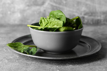 Bowl with fresh spinach leaves on grunge background