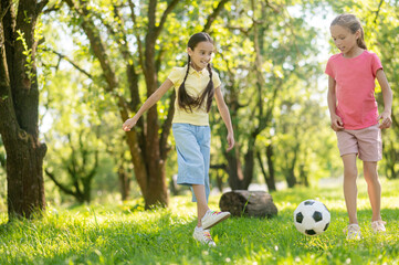 Two younger girlfriends playing soccer on lawn