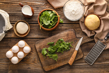 Fototapeta na wymiar Ingredients for preparing spinach tart on wooden background