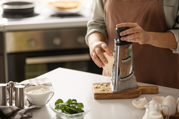 Woman grating cheese for spinach tart in kitchen