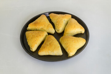 Fish buns are arranged in a round steel baking tray. Homemade delicious Triangular shaped pastry for the family brunch. Buns have risen and baked to perfection.