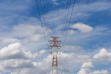 青空と雲の中に立つ赤と白に塗装された高圧送電塔

