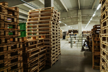 Bunch of wooden pallets in the warehouse. Empty warehouse space with lots of pallets neatly stacked in the factory plant. Indoor warehouse with no people, distribution and logistics, supply